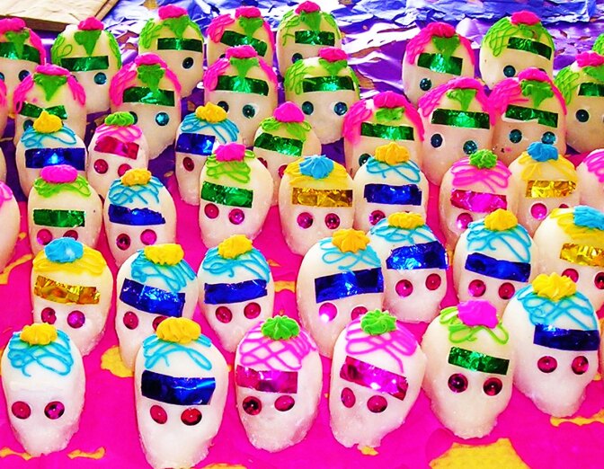 A pink table is covered in vividly decorated tiny sugar skulls.