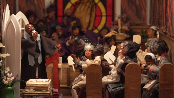 A miniature diorama depicts a scene of Martin Luther King Jr. standing at a podium, delivering a sermon to about a dozen clay churchgoers sitting in pews.