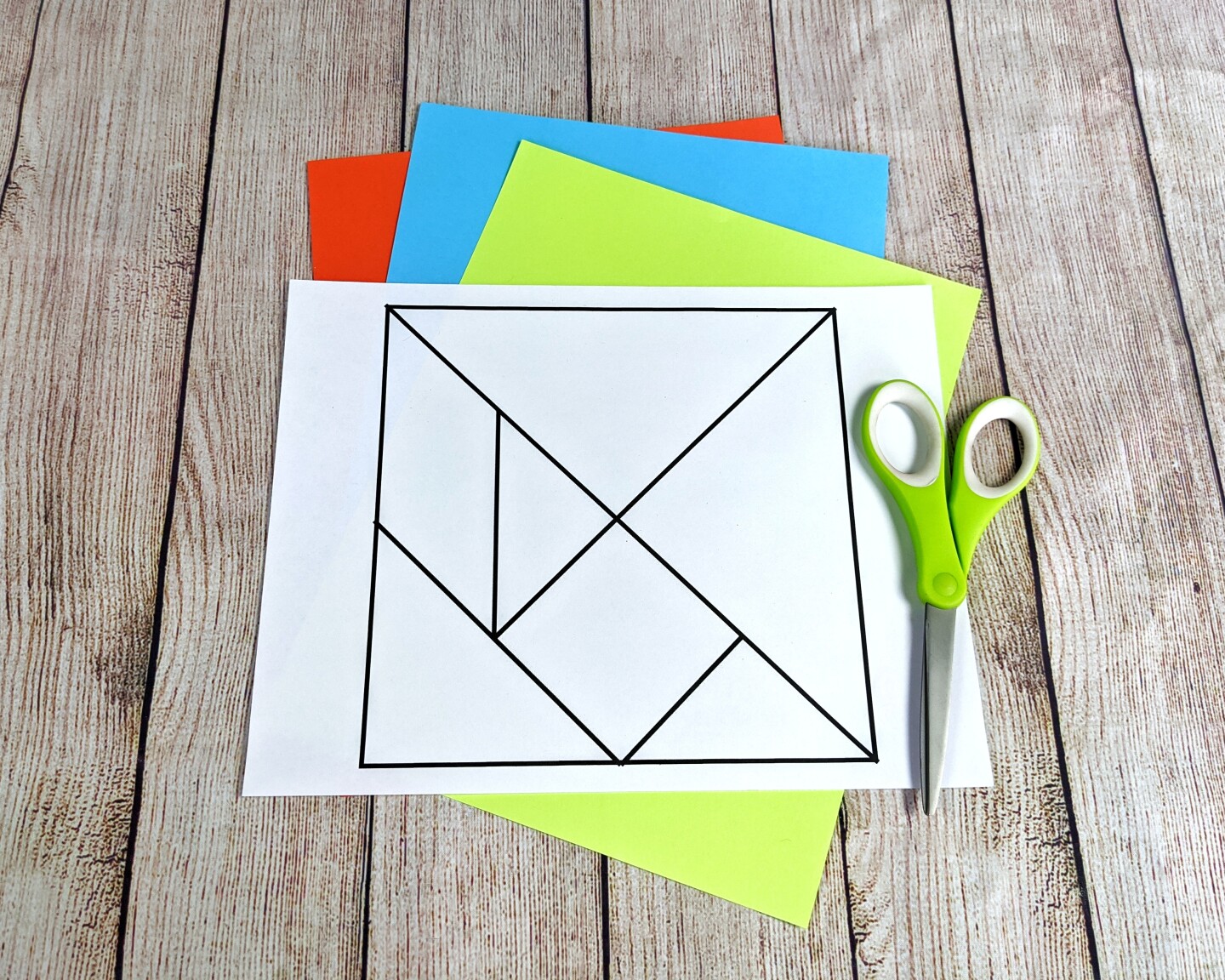 A template for a tangram is laid out on a table alongside some scissors and colorful paper.