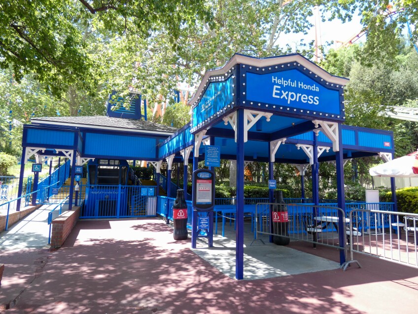 The entrance to the funicular features dark blue wooden posts and a royal blue roof. The front of the entrance reads, "Helpful Honda Express" in white paint over the royal blue structure. Royal blue railing zig zags beyond where people would line up for the ride.