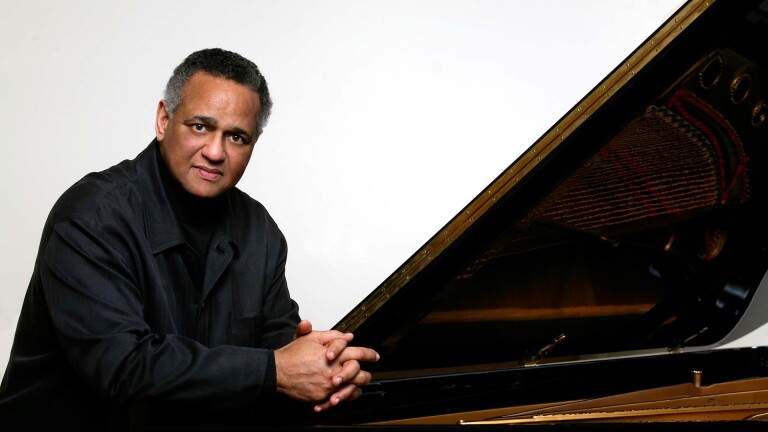 A publicity shot of André Watts sitting by a piano | Courtesy of Pacific Symphony