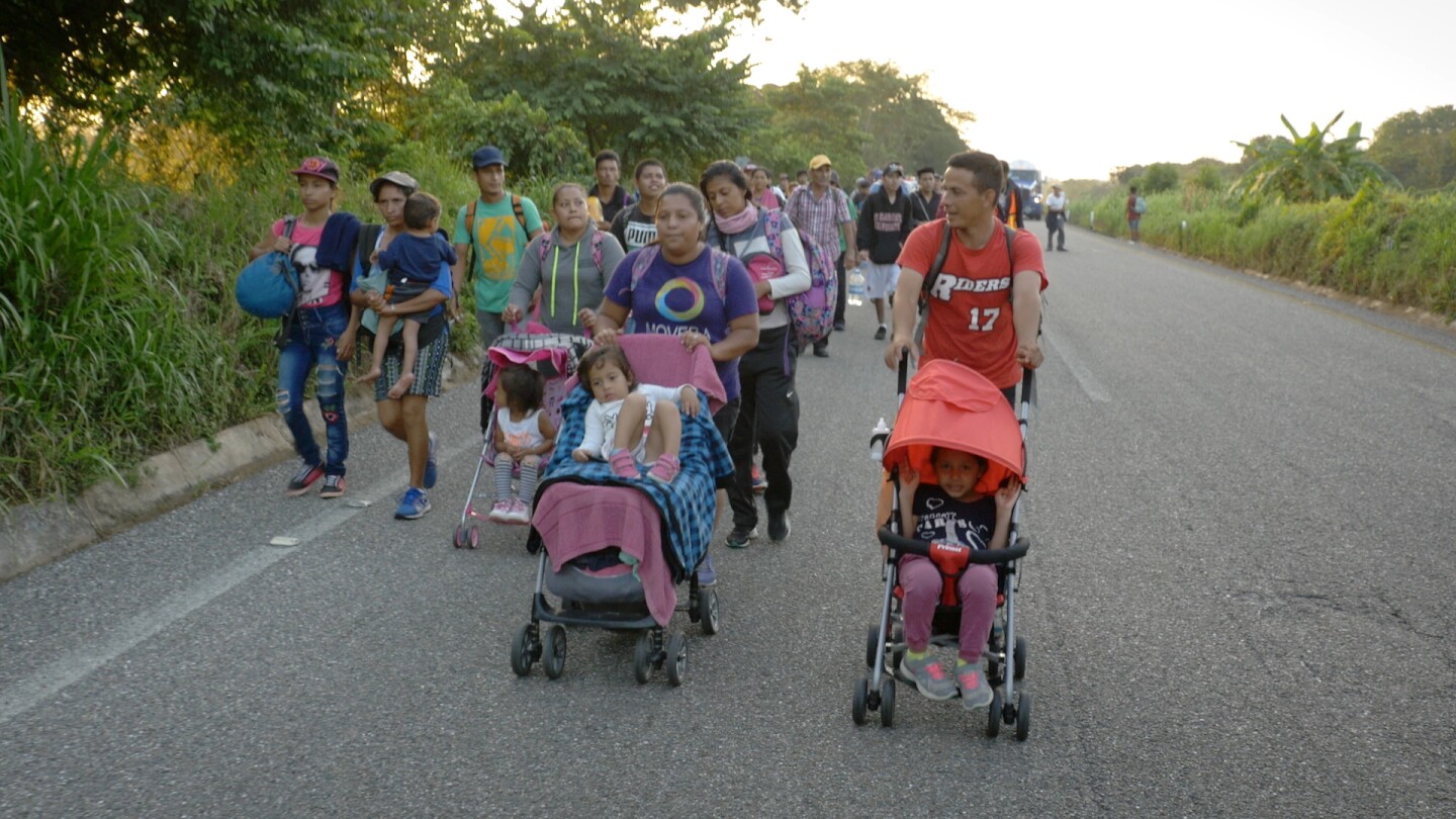 A group of migrants in a caravan push strollers on the road.