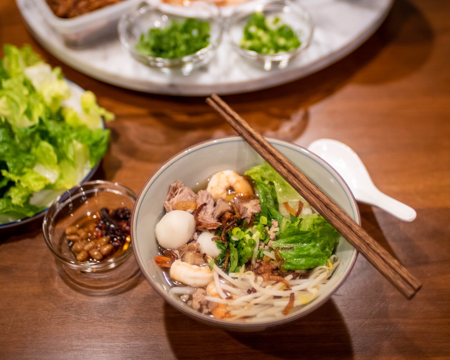 A bowl of Teochew noodles served with pork and seafood in broth garnished with fresh vegetables.