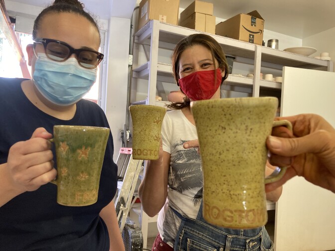 Three women holding cups and face masks on.