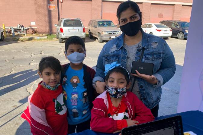 A young family wearing masks smiles at the camera while in front of a table.