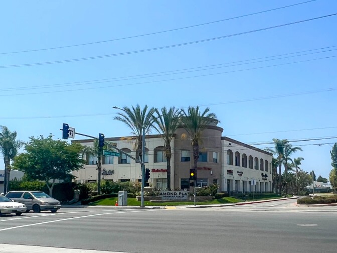 A commercial street corner at a major intersection. Cars wait at the light. The commercial plaza has a sign that reads, "Diamond Plaza."