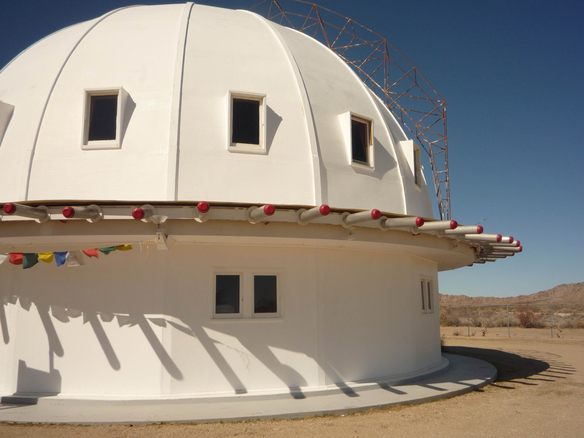 A white dome building in the middle of a desert. Small rectangular windows are evenly spaced out on the dome.