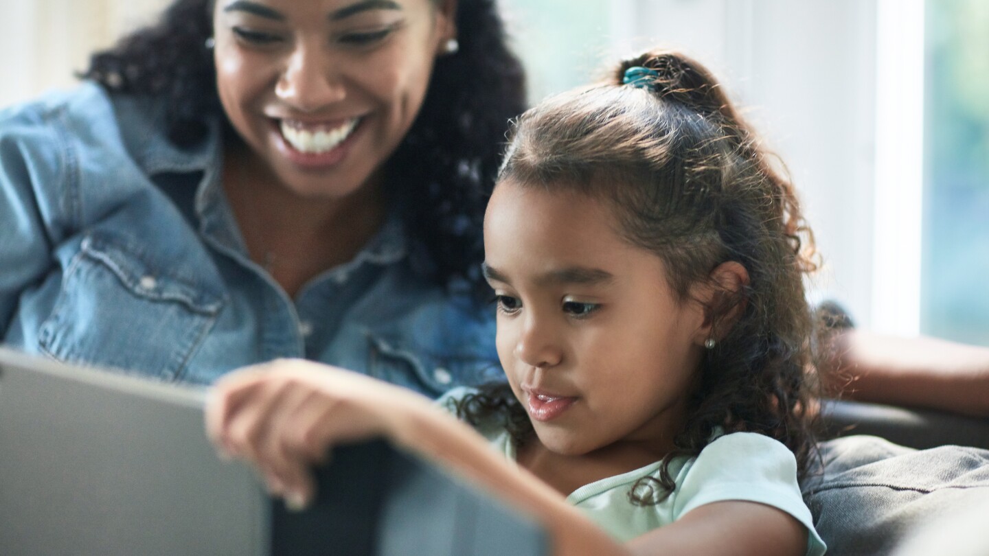 Mother sitting by daughter using digital tablet