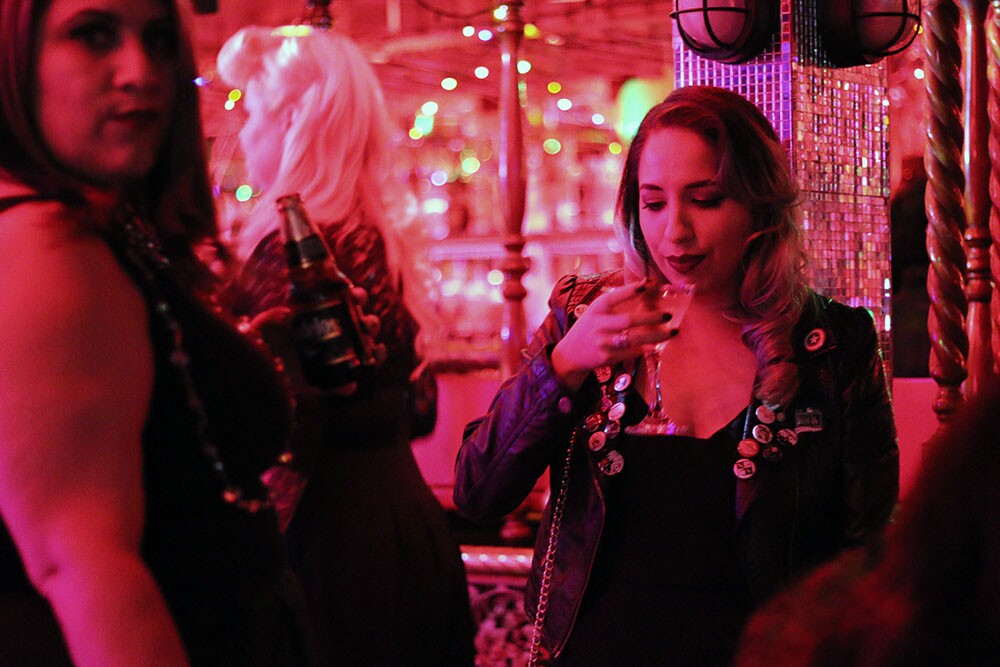 Women stand around the dance floor under red lighting with drinks.