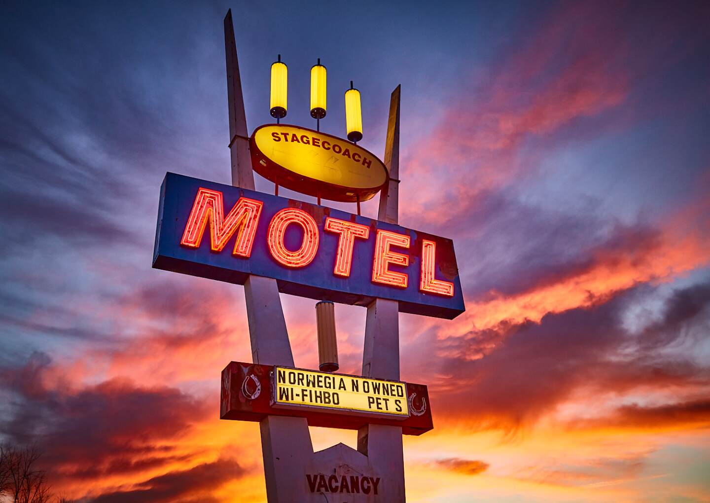 A neon "Stagecoach Motel" sign against a sunset background.