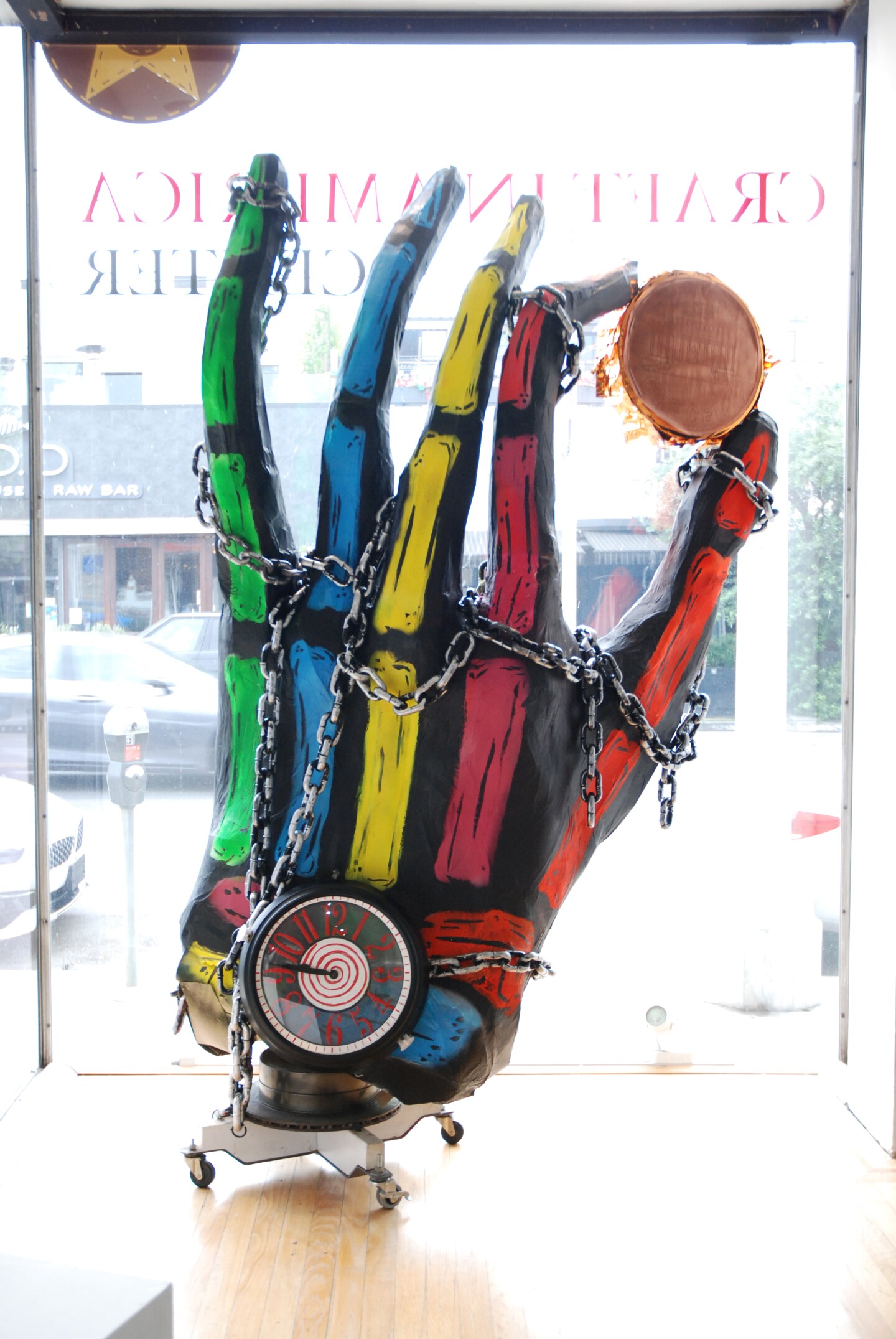 A hand-shaped piñata holds a coin up to a window.