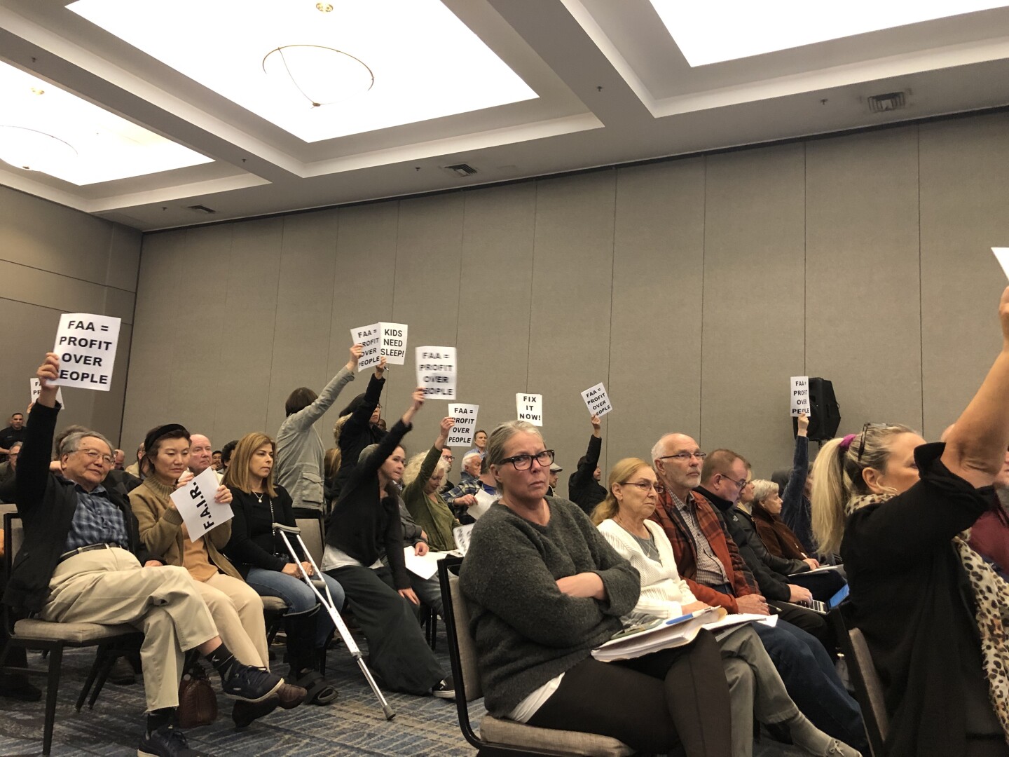 People holding signs against F.A.A while sitting in a meeting about Burbank Airport Noise