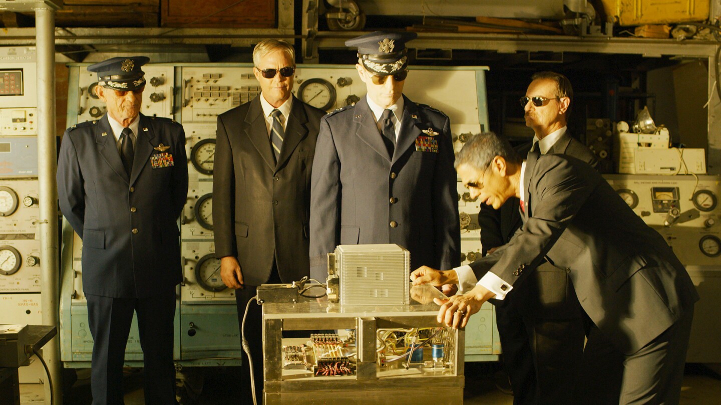 Government officials examine a box lying on a table in front of them.