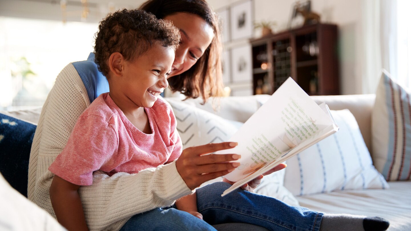 A woman and a little boy read together on a couch