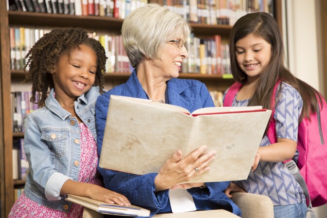 A librarian and two little girls read a book together.