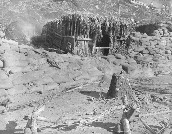 A simulated battle scene with a nipa hut and sandbags.