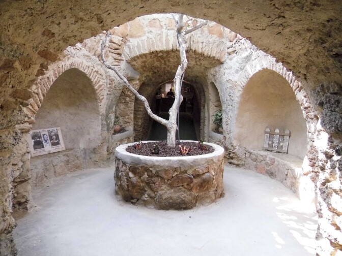 A network of tunnels lead to a tree in the center of an open pocket of space. Above sunlight streams in through a hole for light and the tree to pass through.