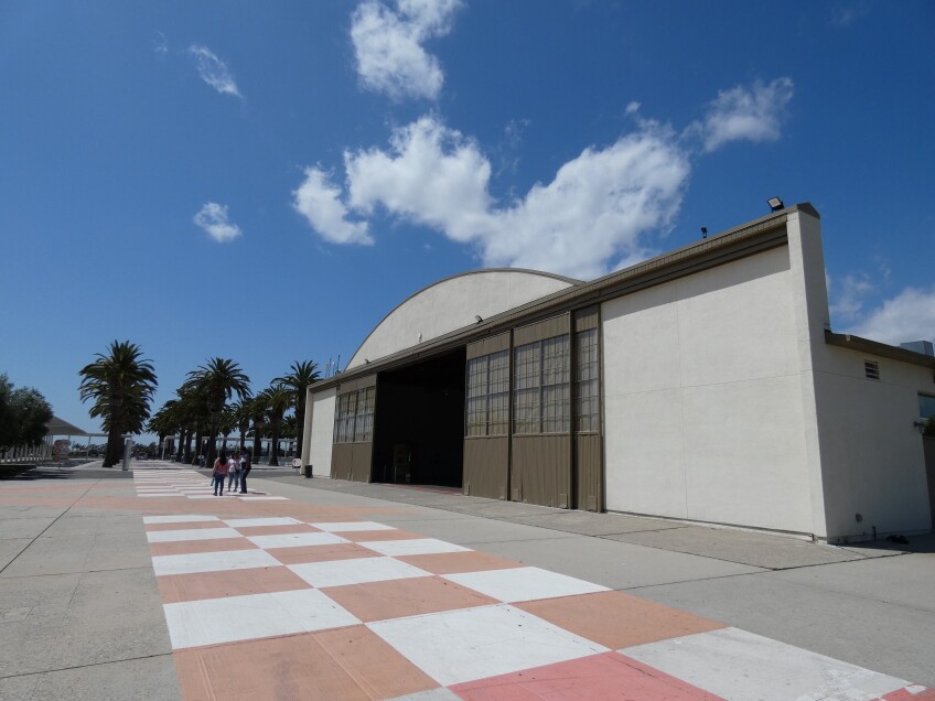 An airplane hangar opens to an orange and white checkered painted paved walkway. 