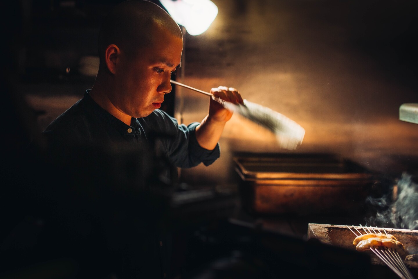 Chef Jon Yao prepares two bite-sized fish skewered over a smokey box.