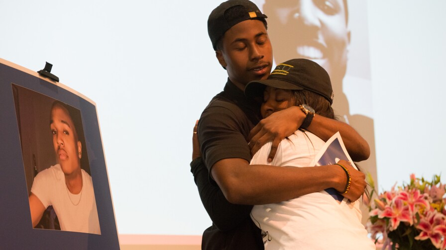 Two people hugging at memorial with photo of deceased next to them | Still from SoCal Connected, "Who Killed Josiah?", Courtesy Mark McKenna