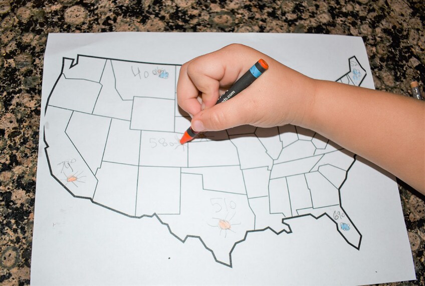 A small child's hand draws different temperatures on each state in a map of the United States.