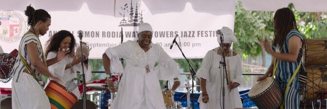 A group of performers dance and drum at the Day of the Drum Festival at the Watts Towers Arts Center. | Still from "Southland Sessions" " Watts Towers Festivals"
