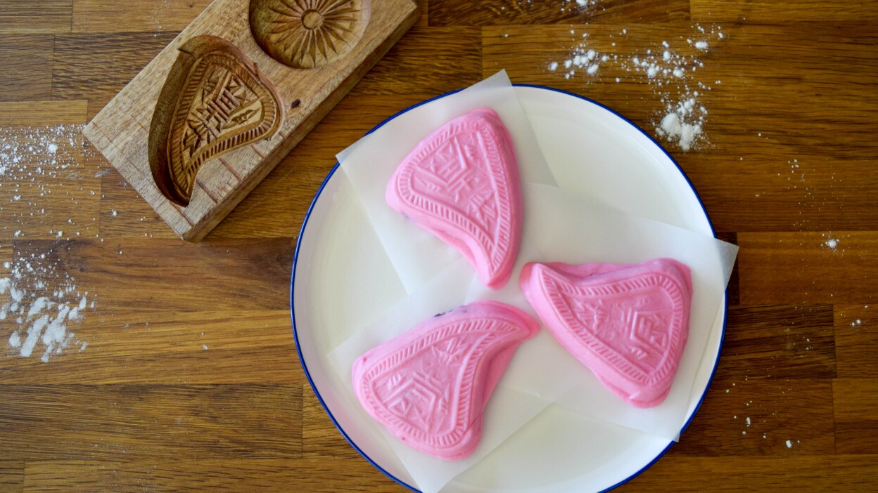 Three pieces of ang to gue, a traditional savory pink peach-shaped rice dough, sit on a plate.