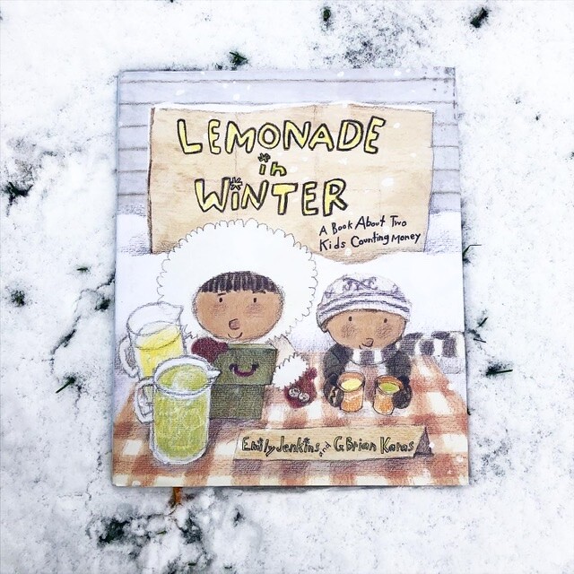 The children's book “Lemonade in Winter: A Book About Two Kids Counting Money,” written by Emily Jenkins and illustrated by G. Brian Karass lying in the snow. The cover features an illustration of two children wearing winter coats as they sell lemonade.