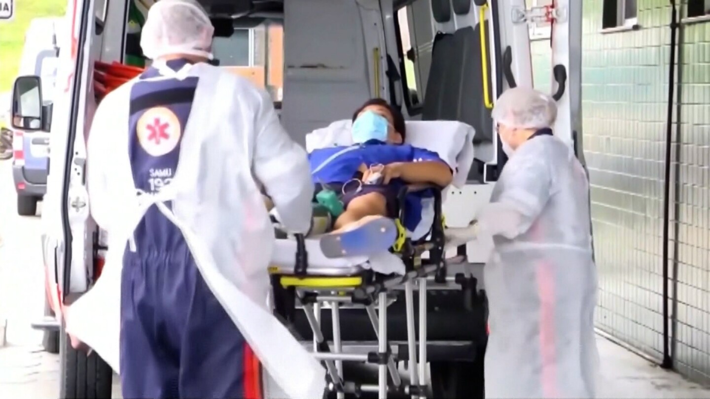 Healthcare workers help a man lying on a gurney at the back of an ambulance.