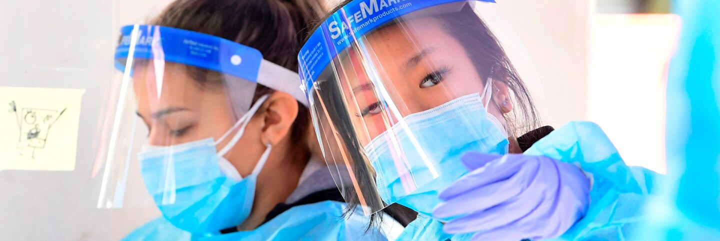 Testing Center Specialits fully dressed in personal protective equipment assist people checking in for a coronavirus test at Union Station in Los Angeles, California on November 13, 2020. | FREDERIC J. BROWN/AFP via Getty Images