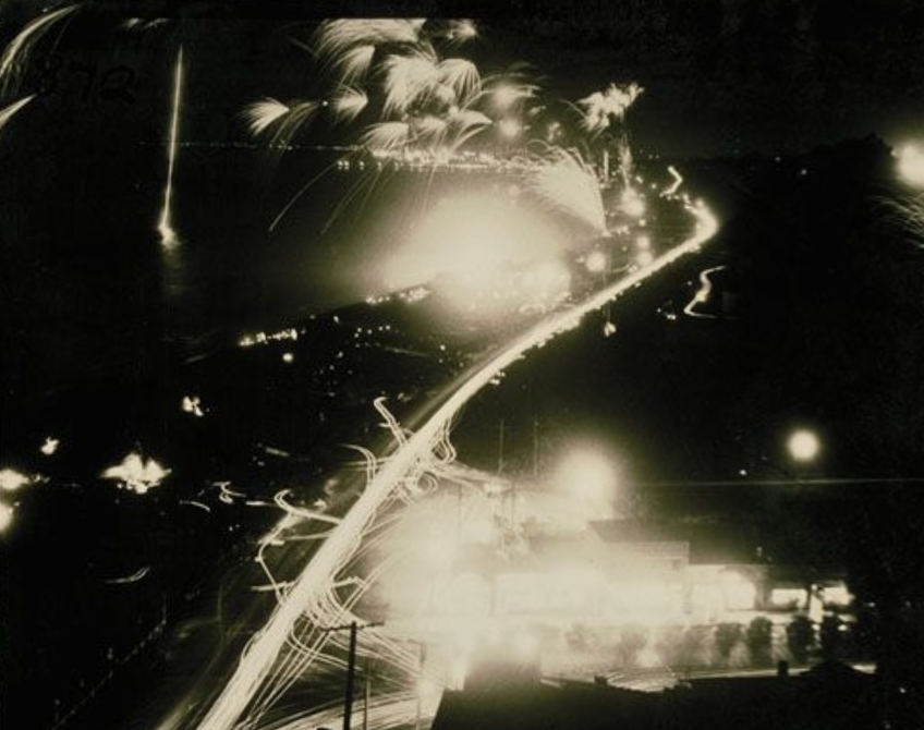 Long exposure photograph of fireworks along the coast w/lights from automobile traffic