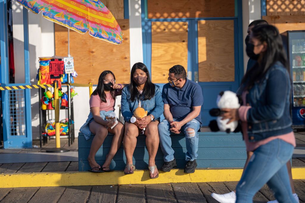 A family wearing masks sits on a bench at the Santa Monica Pier amid the coronavirus pandemic on April 20, 2021 in Los Angeles, California.