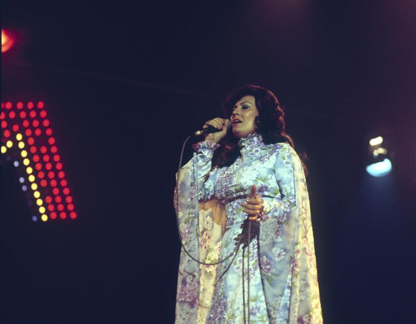 Loretta Lynn sings into a microphone while standing on stage