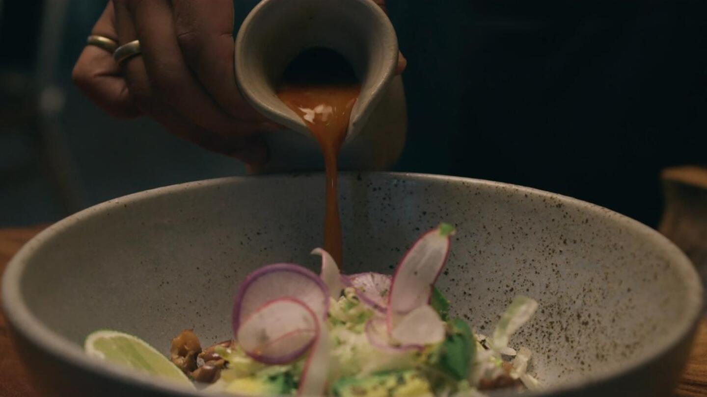 Pozole broth being poured tableside at restaurant El Jardin. | Still from "The Migrant Kitchen"