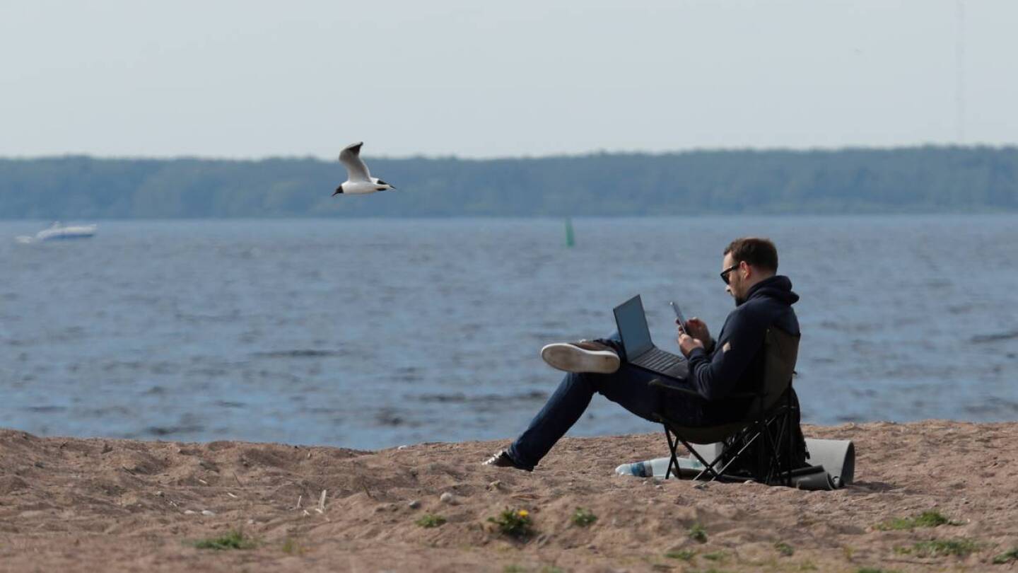 FILE PHOTO: A man uses his smartphone and laptop as he sits on the shore of the Gulf of Finland amid the outbreak of the coronavirus disease (COVID-19) in Saint Petersburg, Russia May 27, 2020. | REUTERS/Anton Vaganov