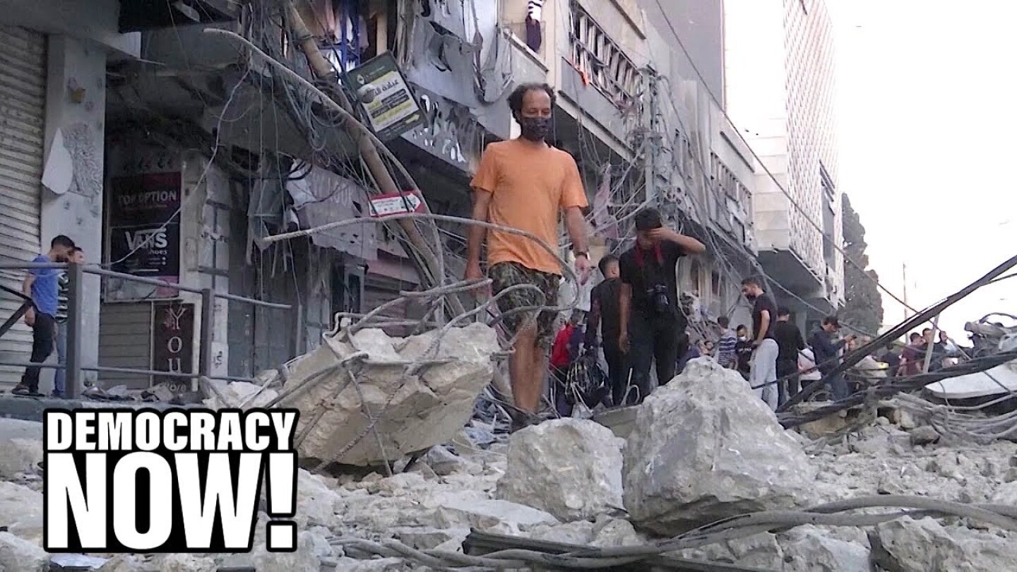 A crowd of people navigate through concrete debris in a city.
