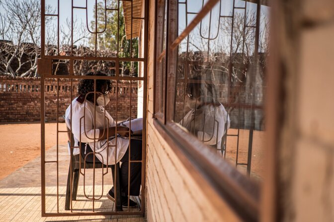 Sister Rachel Asitile (61) is pictured sitting, in accordance with social distancing measures, outside the home of a patient who tested positive for COVID-19 to do a follow up assessment. | Thomson Reuters Foundation/Gulshan Khan