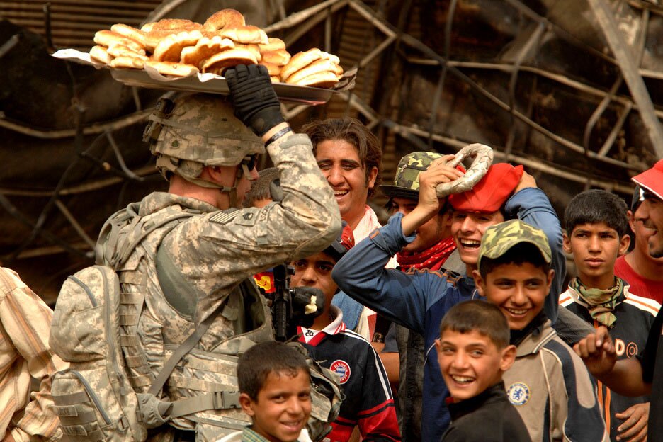 A group of Iraqi children look on as a U.S. Soldier practices balancing a plate of bread on his head in the Jameela market area of the Sadr City district of Baghdad, Iraq. | Tech. Sgt. Cohen A. Young / United States Forces Iraq/ Flickr