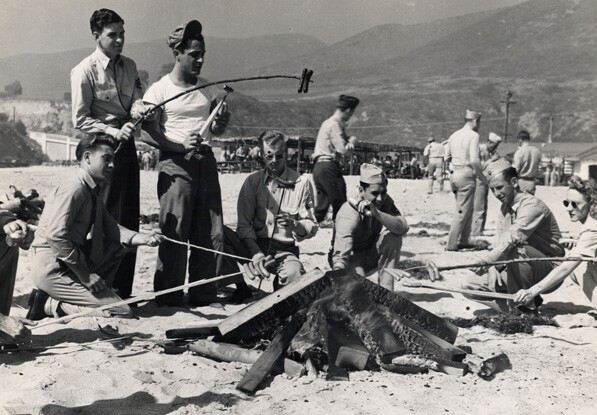 Photograph of Junamay Coffey and other Marines cooking over a campfire at Laguna Beach, 1945. On the backside Coffey wrote: Laguna Beach, CA, 1945. Operation...46, Weiner Roast.