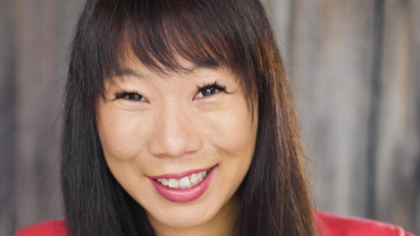 Kristina Wong smiles at the camera. She is wearing a red sweater with a yellow top.