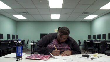 Night school student Melissa intently writes on a piece of paper in an empty computer lab. | From "Night School"