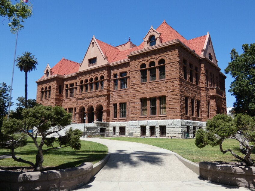 A Richardsonian Romanesque building made of Arizona red sandstone. The grounds surrounding the building is covered in green grass and trees. 