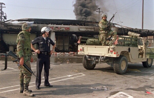 National Guardsmen and a police officer take up security positions in front of a burned and looted shopping center on May 1st, 1992 in central Los Angeles. | Photo: HAL GARB/AFP/Getty Images)