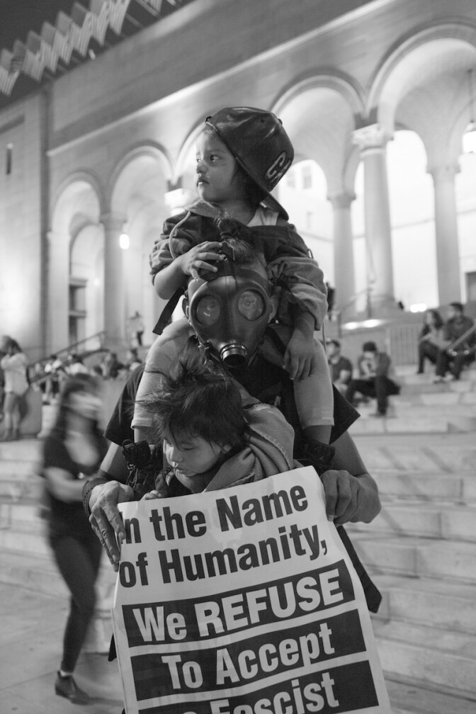 Man in gas mask with two children and a protest sign | Rafael Cardenas