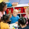 Small children at a preschool center. A teacher holds up one finger as she counts.