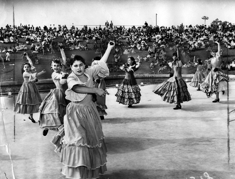 Women in tiered skirts dancing during Cinco de Mayo at Belvedere Park while crowds look on.