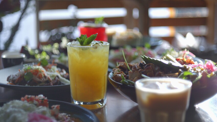 A spread of food on a wooden table features a colorful salad, Korean short rib tacos and a yellow iced beverage.