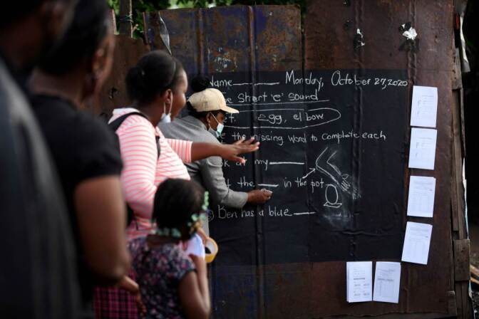 Educator Taneka Mckoy Phipps writes a lesson on a blackboard painted on a zinc fence, in a low-income neighbourhood, during the coronavirus disease (COVID-19) outbreak in Kingston, Jamaica October 27, 2020. October 27, 2020. | REUTERS/Gladstone Taylor