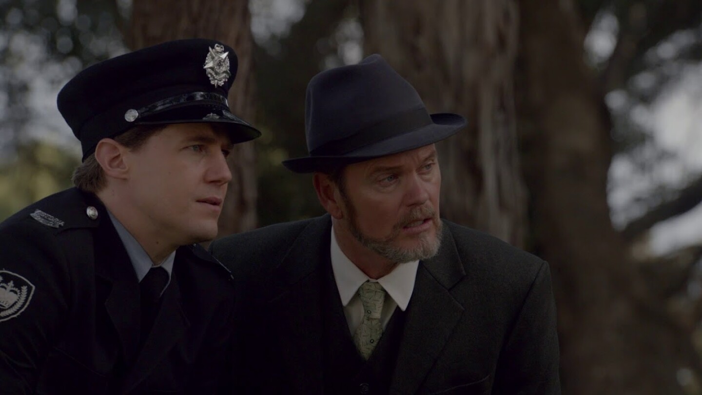 Scene from The Doctor Blake Mysteries: Craig McLachlan standing with officer looking off screen
