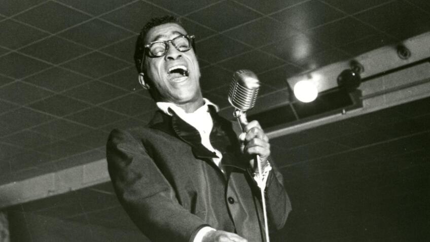Sammy Davis, Jr. sings into a microphone.